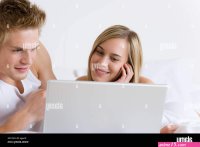 Young couple relax in bed with laptop lying down Stock Photo